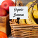 A basket of organic bananas with American Metalcraft Mini White Chalk Cards on a counter.