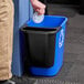A black Rubbermaid oval wastebasket with a white lid.