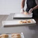 A person wearing gloves prepares pastries on white plastic Channel platters.