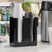 A black two-section countertop organizer holding stacks of disposable cups and lids.