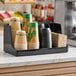 A black three-section countertop organizer holding disposable cups, lids, and napkins.