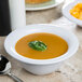 A white Carlisle melamine nappie bowl filled with soup with a spoon next to it.