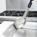 A hand holding a Vollrath Black Solid Oval Spoodle over a pan.