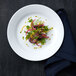 A Oneida Botticelli bright white porcelain plate with salad and vegetables on it.