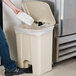 A hand putting a plastic container into a beige rectangular Lavex step-on trash can.