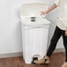 A woman throwing a paper towel into a white Lavex rectangular step-on trash can.