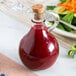 A Tablecraft olive oil bottle with a cork on it next to a plate of salad.