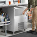 A Manitowoc undercounter ice machine on a counter in a bar with a person putting ice in a glass.