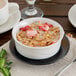 A Oneida cream white china bowl filled with cereal, strawberries, and milk on a table.