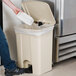 A hand putting a plastic container into a beige Lavex rectangular step-on trash can.