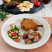 A plate of food with a piece of meat, crackers, and salami on a white Oneida Espree china plate.