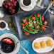 A Oneida cream white china rim deep soup bowl filled with blueberries and strawberries on a table with a plate of food.