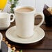 A close-up of a Oneida cream white china mug filled with brown liquid on a white plate.