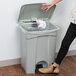 A woman using her foot to open a Lavex rectangular step-on trash can in a room with a salad bar.
