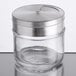 A Tablecraft glass spice shaker with a silver metal lid on a table.