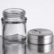 A Tablecraft glass spice shaker with a metal adjustable lid.