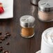 A Tablecraft glass spice shaker with brown powder on a table.