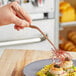 A hand using Mercer Culinary rose gold offset tip plating tongs to plate food.