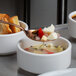 A Mercer Culinary rose gold perforated bowl plating spoon holding a piece of bread over a bowl of soup.