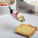 A Mercer Culinary stainless steel slotted bowl plating spoon holding a piece of bread over a bowl of soup.