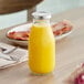 An Acopa glass bottle of orange juice on a table.