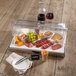 A Frilich clear plastic roll top dome cover on a tray of food and wine on a table.