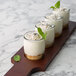 A row of Acopa 4 oz. beer tasting glasses filled with white desserts on a wooden board.