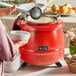 A woman holding a white bowl of soup over a red Avantco soup kettle.