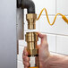 A hand holding a yellow Regency gas hose connected to a brass pipe.
