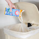 A hand pouring Arm & Hammer trash can deodorizer into a trash can.