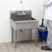 A man with a mop using a Regency stainless steel standing mop sink.