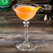 A Libbey coupe cocktail glass with orange liquid in it.