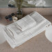 A stack of white Oxford Vicenza hand towels on a white bathroom counter.