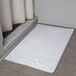 An Oxford Reserve white 2-ply combed cotton bath mat with a dobby border on a tile floor.