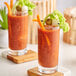 A close up of two glasses of V8 Original vegetable juice with olives and vegetables.