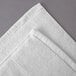 An Oxford Vicenza Bianco white bath mat with a Dobby border on a gray surface.