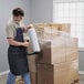 A man in an apron using a Universal hand dispenser to wrap boxes in plastic.