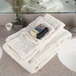 A stack of Oxford Vicenza Avorio bath towels with a dobby border on a white bathroom counter.