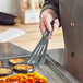 A hand using a Mercer Culinary gray high temperature slotted turner to cook food on a pan.