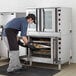 A man wearing an apron putting cookies in a Cooking Performance Group commercial convection oven.