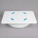 A white Ateco plastic cake turntable with blue circles on it.