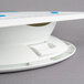 A white Ateco plastic cake stand with blue and white buttons on top.
