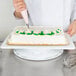 A person using an Ateco Two Sided Revolving Cake Stand to decorate a cake.
