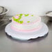 A Wilton cake stand with a cake frosted in pink and green on it.