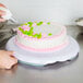 A hand using a pastry bag to decorate a cake on a Wilton plastic cake turntable.