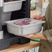 A woman holding a Vollrath stainless steel transport pan filled with food.