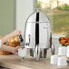 A woman using a Choice stainless steel coffee chafer urn to pour coffee into a white cup on a table.