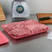 A CKF rose foam meat tray of raw meat on a counter.
