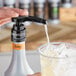 A hand using a Monin concentrated flavoring pump to pour liquid into a glass of ice.