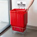 A person holding a red Regency shopping basket with plastic handles.